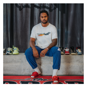 Tevin Haye, Founder of Unavailshop, sitting on a cement blog with displayed sneakers laid out on either side of him. Photo by Yoni Sambo.