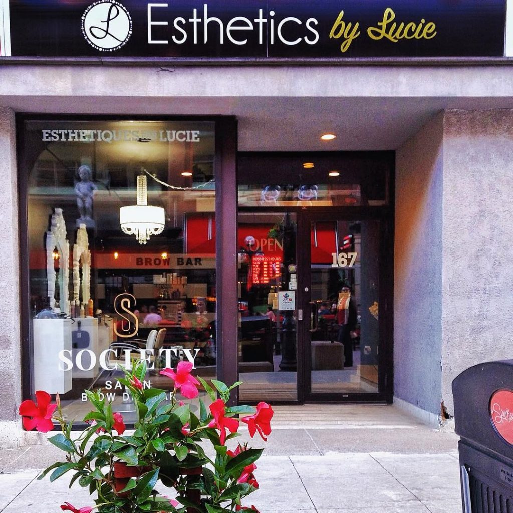 The Esthetics By Lucie Location - at 167 Sparks Street - with red flowers out front of the shop window.