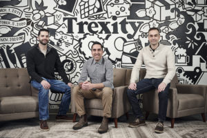 An image of the founders of Trexity - all seating and smiling in front of a wall, vividly branded for Trexity in a black and white design.
