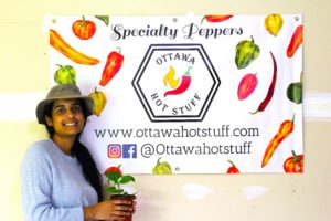 Owner of Ottawa Hot Stuff, and Summer Company graduate Ayesha Iqbal standing in front of a sign with contact information. 