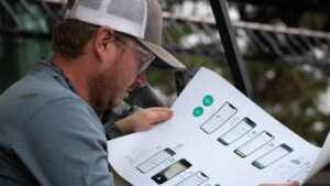 Danny Ottenbreit - a grain producer in Saskatchewan reviews information on the Combyne App during product trials. He's on the left, wearing a hat and glasses, while looking at a printout of the functions of the app.