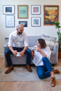 Sarah and Ryan Gencarelli, owners of wild idea co. seated and smiling in a living room setting.