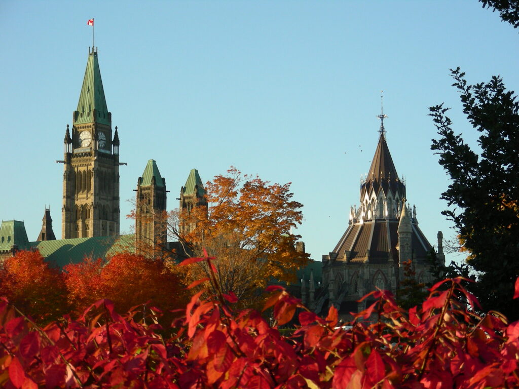 A view of the Parliament Buildings in Ottawa through red fall trees.