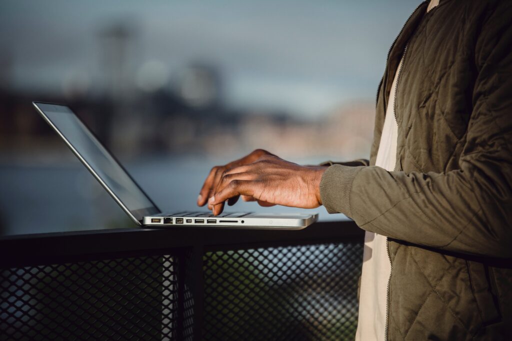 Close up of a person typing on a laptop outside on a terrace.