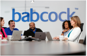 the Babcock team seated in front of their laptops at a round boardroom table, collaborating. 
