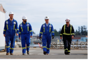 Babcock employees walking in a line across what appears to be a runway wearing site suits and hardhats.