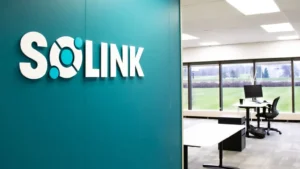 The Solink logo appears on a blue coloured wall, with a desk inthe background in an open layout in front of a window.