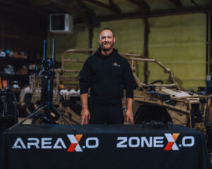 Mike Nelson - founder of Tactiql standing behind a presentation table labeled in front with Area X.O's branding.