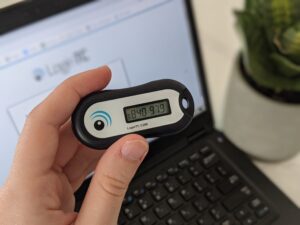 A person holds a piece of technology in front of a lap top screen. 