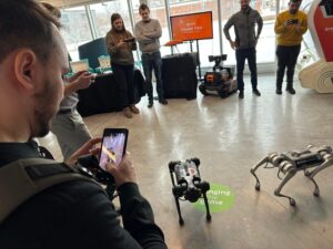 People gather together to watch and take photos of robots in action at an indoor event. 