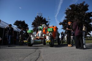 A vehicle is positioned in the middle of a group of people gathering outdoors to network. 