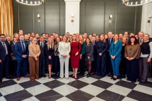 A group gathers for a photo inside a room with a checkered floor. 