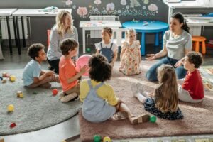 A group of children and care providers gathers on a carpet at what appears to be a childcare centre.