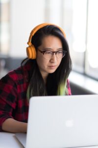 A woman sits at a laptop working by a window. 