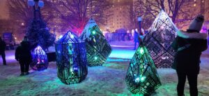 People walk through a colourful art installation in the night. 