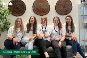 The team for Knak, seated on a bench and playfully posing for a photo, laughing together. 