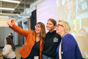 Comeback Snacks Founder Emily O'Brien joins two women for a photo in front of the stage at an Invest Ottawa International Women's Month event. 
