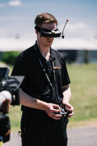 A drone operator wearing goggles operates a drone outside.