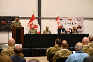 Lieutenant Colonel Jayme Leclerc serving as master of ceremonies for the Red Cobalt event at Area X.O Killaloe, featuring a panel (left to right) Lieutenant General Darcy Molstad, General Jennie Carignan, Chief of the Defence Staff; , commander of Canadian Joint Forces Command, Honourable David J. McGuinty, Minister of National Defence; and Sonya Shorey, President and CEO of Invest Ottawa and Area X.O