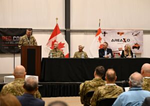 Lieutenant Colonel Jayme Leclerc serving as master of ceremonies for the Red Cobalt event at Area X.O Killaloe, featuring a panel (left to right) Lieutenant General Darcy Molstad, General Jennie Carignan, Chief of the Defence Staff; , commander of Canadian Joint Forces Command, Honourable David J. McGuinty, Minister of National Defence; and Sonya Shorey, President and CEO of Invest Ottawa and Area X.O
