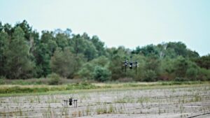 Two drones are visibile along an old unused runway, where grass is growing through. 