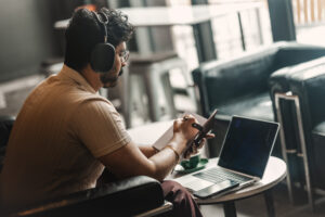 A person wearing a communications headset working away on multiple devices while having coffee.